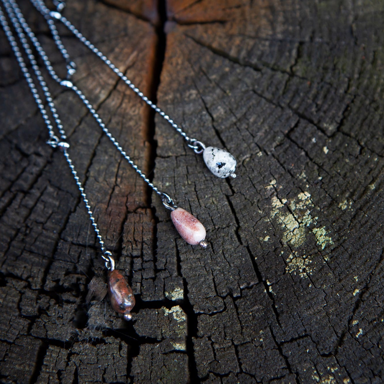 Närbild av STRAND Droppe halsband med droppformade stenar mot en väderbiten träyta