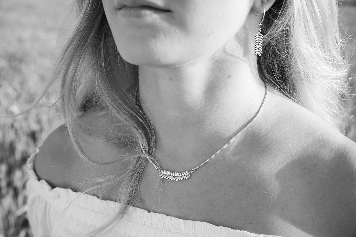 Svartvit bild av en kvinna som bär RÅG halsband och örhängen i silver i en naturmiljö