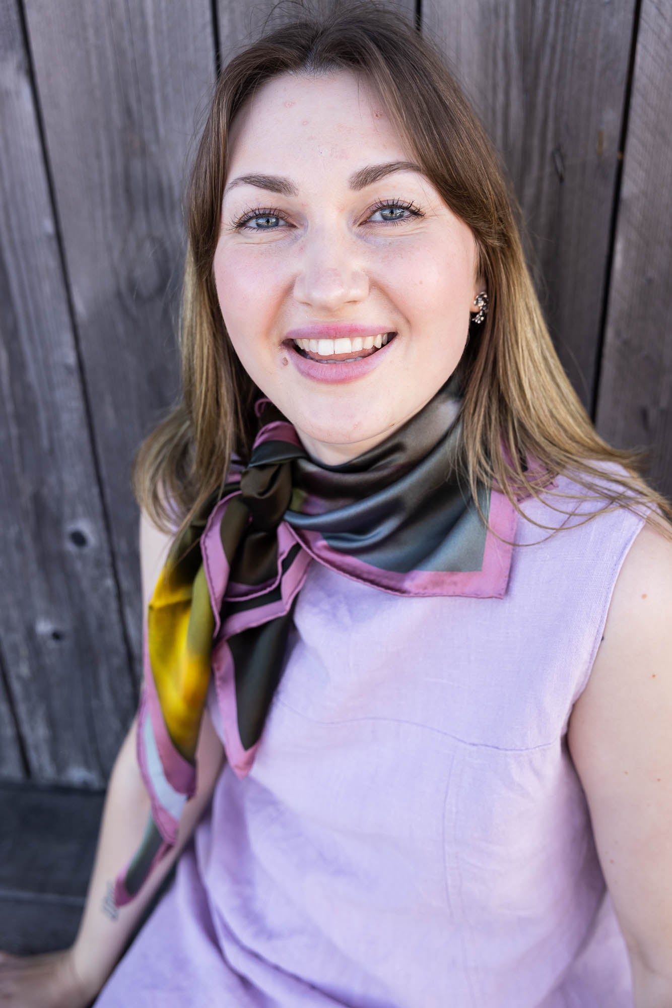 Portrait of a woman wearing the Äppelblom scarf tied at the neck with vibrant multicolor satin fabric and lavender top
