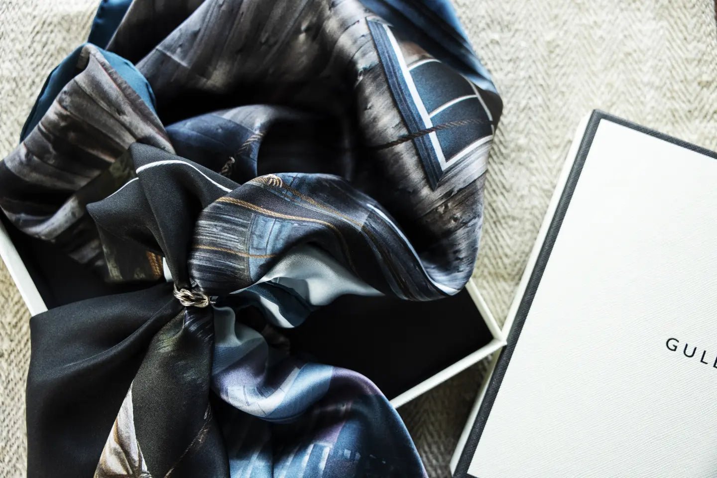 Hemma Hamn silk scarf in blue gray tones tied with a silver ring inside a gift box