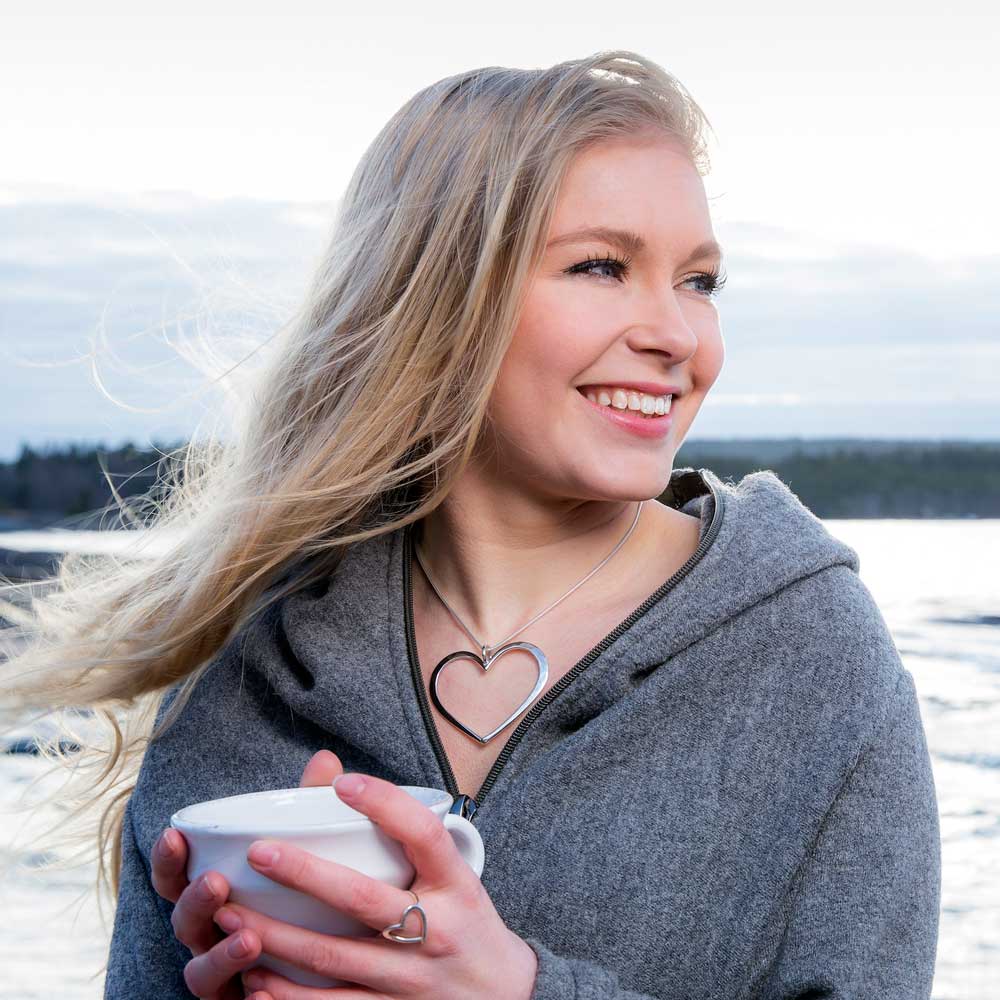 Kvinna vid havet bär ett stort silver hjärtformat halsband