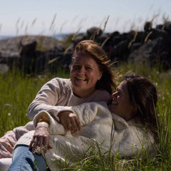 Two friends lying in a grassy field wearing a silver heart pendant necklace.