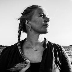 Portrait of a woman by the sea wearing STORMSKÄRS MAJA S silver pendant necklace, with braided hair.