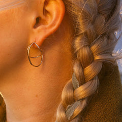 Ear close up wearing STORMSKÄRS MAJA FEST 18K gold hoop earring with braided hair in sunset light.