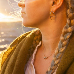 Close up of STORMSKÄRS MAJA S 18K gold necklace with a small pendant on a model during sunset.