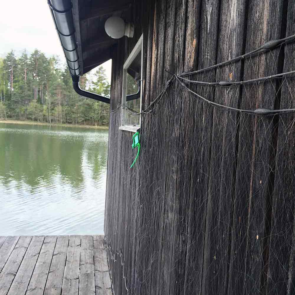 Grön slipsklämma fästad i en trävägg bredvid ett fisknät vid sjön