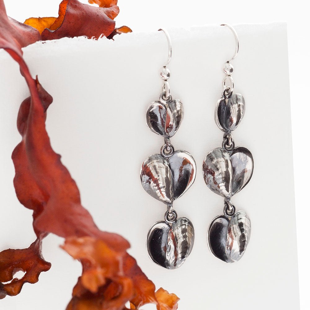 Close up of two silver heart drop earrings with three linked hearts against a white background