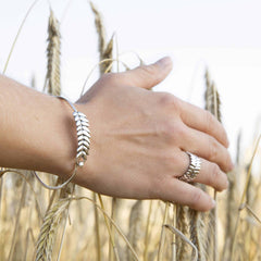 RÅG ROBUST ring i silver med cirka 8 mm bred band visas på hand med vetefält i bakgrunden