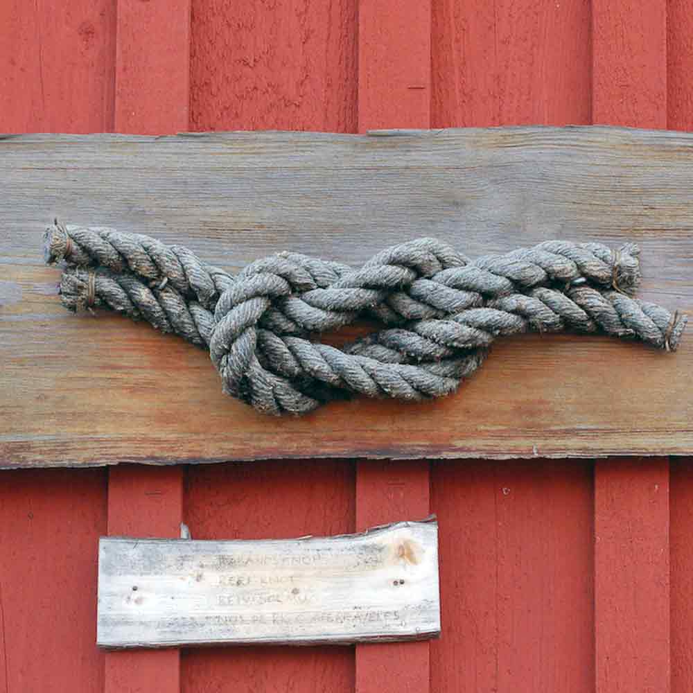 Tjockt segelsnöre i råbandsknop knuten i väderbiten trävägg med röd bakgrund