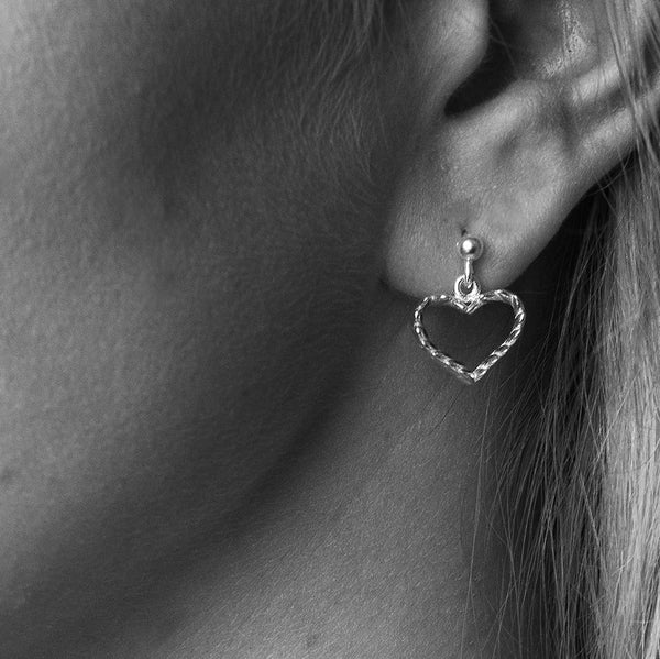 Close up of a silver heart shaped stud earring worn on the earlobe