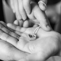 Råghjärta halsband i silver hänge ligger i handflata med kedjan släppt över handen