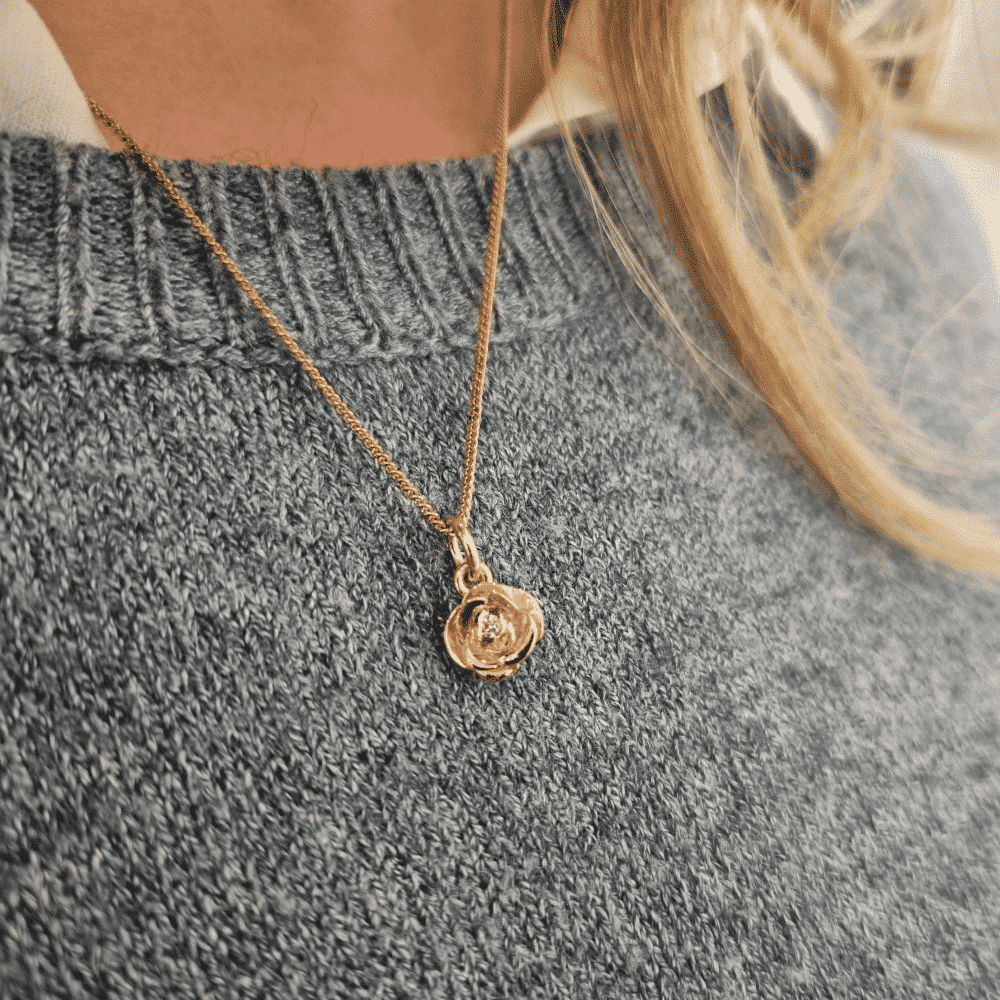 Person bär ett 18K guld Ros halsband med diamant mot en grå stickad tröja.