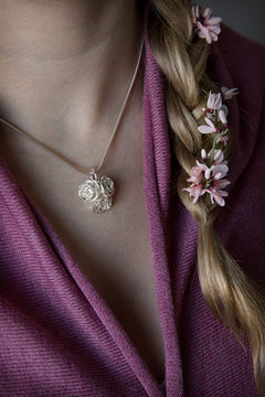 Silver necklace with three rose pendants on a slim chain worn near the neckline.