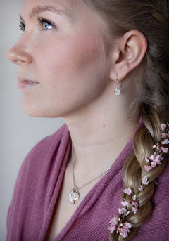 Profil av kvinna i profil som bär rosformade silversörhängen och ett rosformigt hänge på silverhalsband