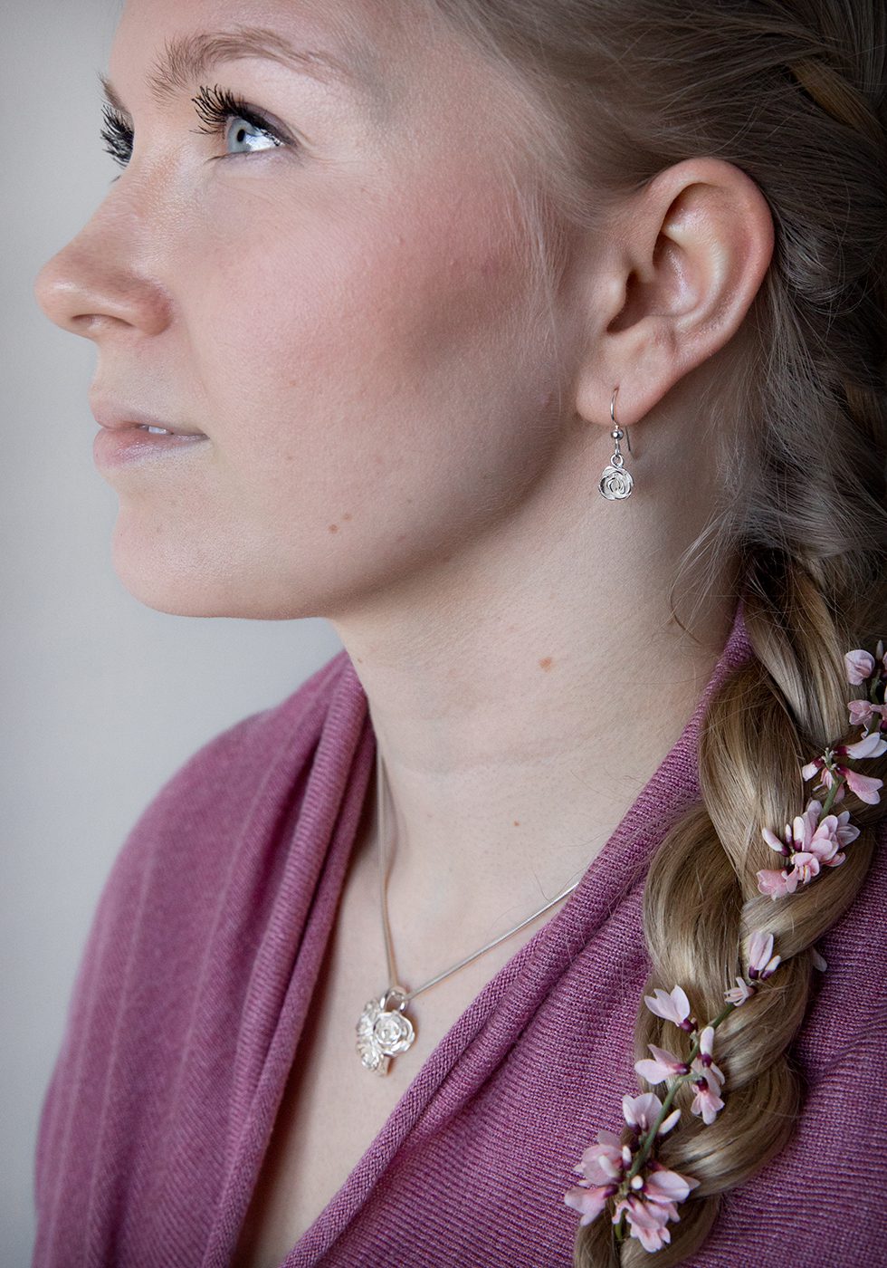 Silver rose pendant drop earring worn by a woman in profile.