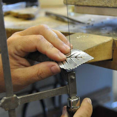 Hands shaping a leaf shaped 925 sterling silver pendant for a BJÖRK XL halsband on a jeweller's bench