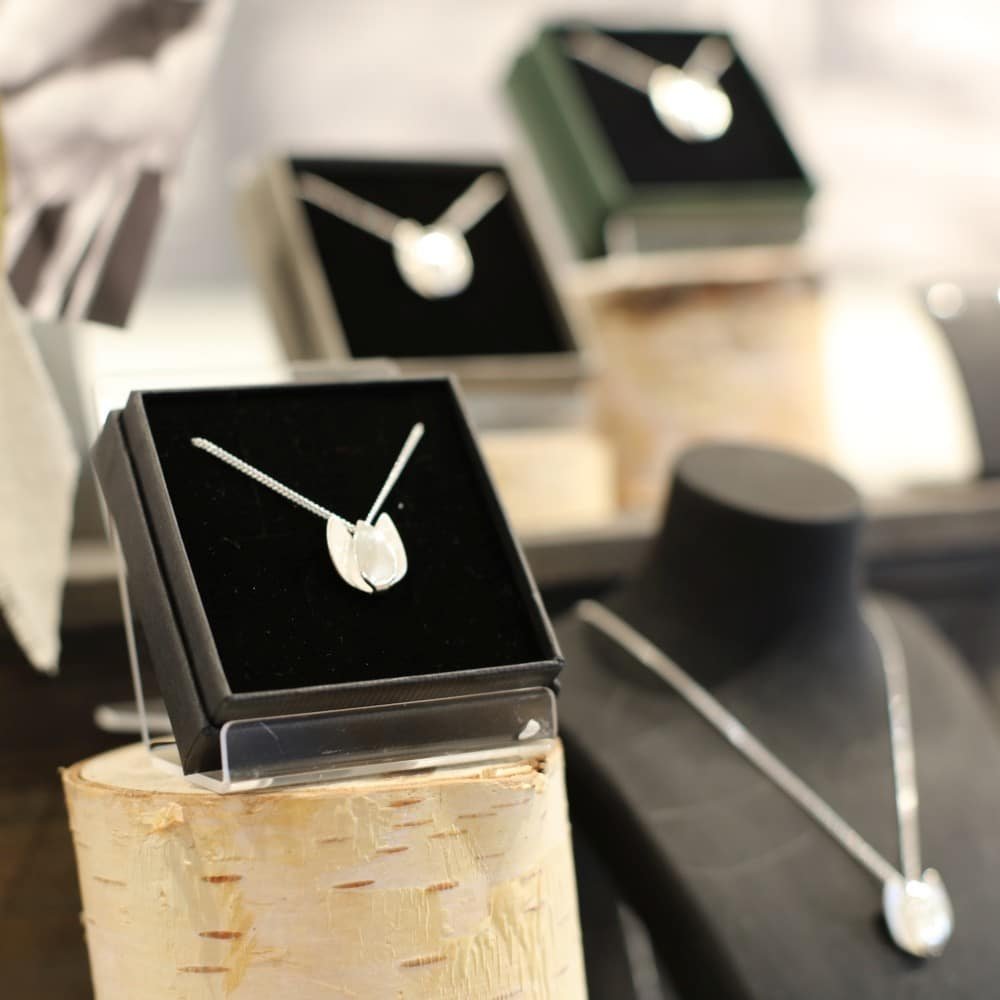 Silver Tulpan Nova pendant necklaces displayed in black boxes on a stand.