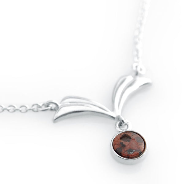 Silver necklace with winglike motifs and a round red granite stone set in silver